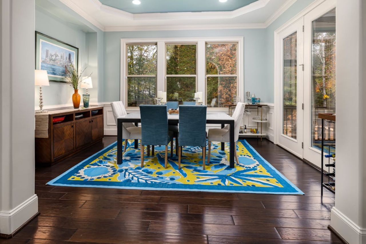 Luxury dining room or office with wood tile, blue upholstered chairs and patterned rug.
